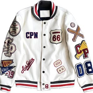 Peut inclure: Une veste universitaire blanche avec une fermeture à boutons-pression, un col, des poignets et un ourlet côtelés rayés. La veste est ornée de divers écussons brodés, dont un écusson Route 66, des battes de baseball, un mégaphone et le texte CPN.