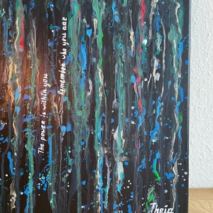 May include: Abstract art canvas with a dark background and vertical streaks of blue, green, red, and white paint. The text "The power is within you, remember who you are" is written in white. Signed "Theia" in the bottom right corner.