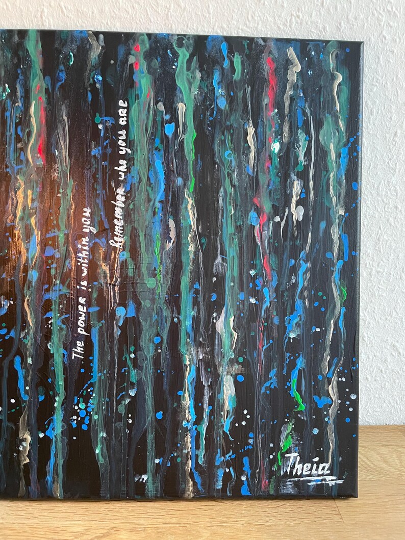 May include: Abstract art canvas with a dark background and vertical streaks of blue, green, red, and white paint. The text "The power is within you, remember who you are" is written in white. Signed "Theia" in the bottom right corner.