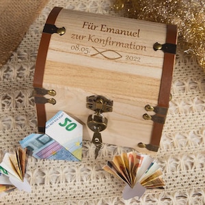 Puede incluir: Un cofre de madera con detalles de cuero marrón y herrajes metálicos. El cofre tiene texto grabado en la parte delantera. Varios billetes de euro doblados están dispuestos alrededor del cofre.