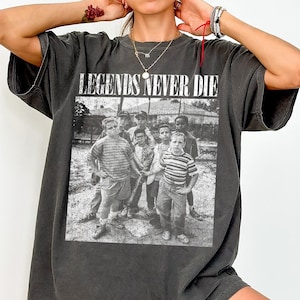 May include: Dark gray t-shirt with the text "LEGENDS NEVER DIE" above a black and white image of a group of boys. The t-shirt is oversized and has short sleeves.