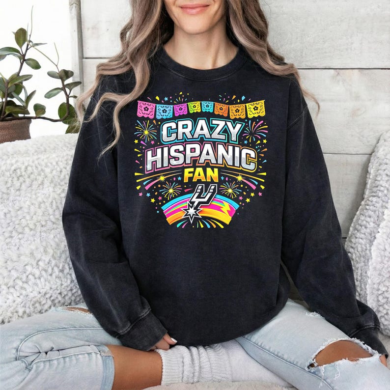 May include: Black crew neck sweatshirt with the text "CRAZY HISPANIC FAN" in colorful lettering. The design includes fireworks, a rainbow, and a logo. The sweatshirt has a vintage wash.