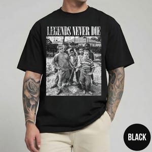 May include: Black t-shirt with the text "LEGENDS NEVER DIE" above a black and white image of a group of boys. The shirt has a crew neck and short sleeves. The word "BLACK" is in a white circle.