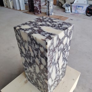 May include: A rectangular pedestal made of polished stone featuring a high-contrast pattern of creamy white and deep dark purple veining. The block has a smooth, reflective surface with sharp edges and a solid, uniform structure throughout its height.