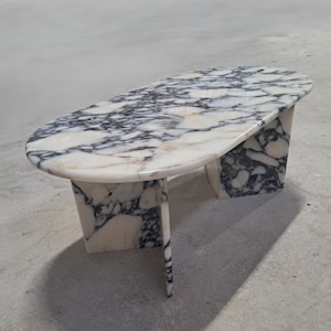 May include: An oval coffee table featuring a polished white and black marble surface with a distinct veined pattern. The table is supported by two thick, matching marble slab legs that extend to the floor, creating a sturdy and cohesive structure.