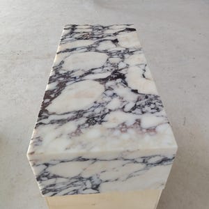 May include: A rectangular bench featuring a polished white marble top with prominent dark purple and black veining patterns. The stone surface displays a smooth, reflective finish with irregular organic shapes throughout the natural stone slab.
