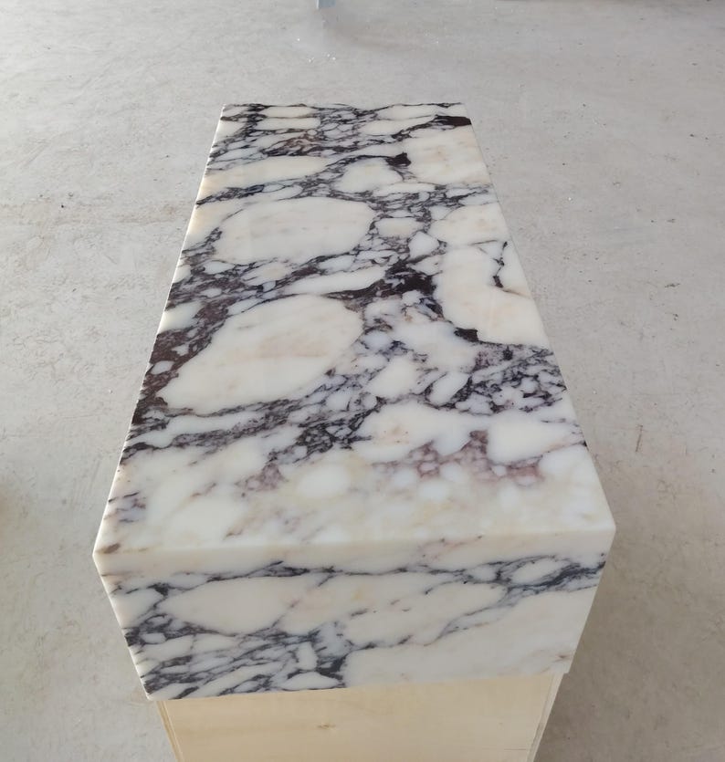 May include: A rectangular bench featuring a polished white marble top with prominent dark purple and black veining patterns. The stone surface displays a smooth, reflective finish with irregular organic shapes throughout the natural stone slab.