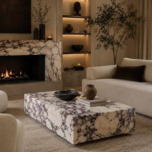 May include: A rectangular coffee table crafted from white and dark purple brecciated marble with a low-profile block design. The surface holds a dark circular bowl and a small brown ceramic vase resting on top of two stacked light gray rectangular books.