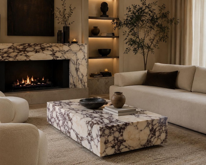 May include: A rectangular coffee table crafted from white and dark purple brecciated marble with a low-profile block design. The surface holds a dark circular bowl and a small brown ceramic vase resting on top of two stacked light gray rectangular books.