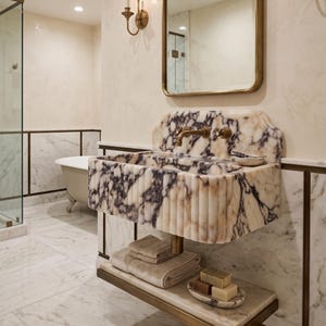 May include: A luxurious bathroom with a marble sink featuring a unique purple and white veined pattern. The sink has a brass faucet and is mounted above a shelf holding towels and soap. A mirror and sconces complete the elegant design.