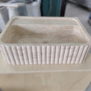 May include: A rectangular, off-white stone sink with a fluted exterior. The sink is set on a light-colored, square base. The design features a central basin and a raised rim, suitable for bathroom or kitchen use.