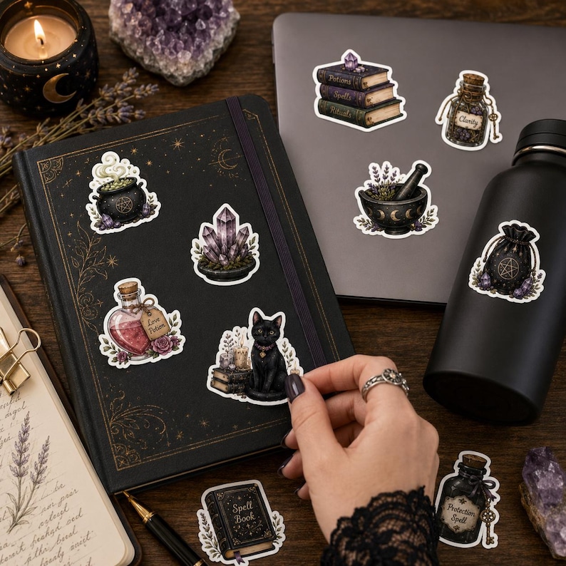 May include: A collection of mystical-themed stickers featuring a black cat, a cauldron, a stack of books, crystal clusters, potion bottles, and a pouch with a pentacle. The stickers are displayed on a black notebook and a dark gray laptop.