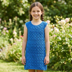 Peut inclure: Robe bleue sans manches en crochet. La robe présente une encolure ronde et un motif de point texturé. La robe arrive au genou et semble être faite à la main. L'arrière-plan est une vue floue d'un jardin avec du feuillage vert et des fleurs.