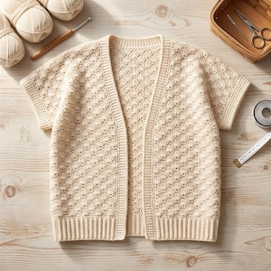May include: Cream-colored, short-sleeved cardigan with a textured, openwork design. The open front sweater is handmade with a ribbed hem and cuffs. Crochet hooks, yarn, and a basket with scissors are in the background.