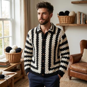Puede incluir: Un cárdigan de crochet negro y crema con un patrón geométrico. El suéter con botones tiene un cuello y se usa con pantalones azules. La imagen está tomada en interiores, con una ventana y muebles de madera en el fondo.