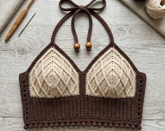 May include: A handmade crochet halter top in brown and cream colors. The top features a diamond pattern on the cups and a ribbed band at the bottom, with small pom-poms. The halter straps are tied with a bow and have wooden beads.