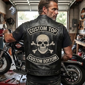 Può includere: Un gilet in pelle nera con una grande toppa ricamata sul retro. La toppa presenta un grafico con teschio e ossa incrociate con il testo CUSTOM TOP arcuato sopra e CUSTOM BOTTOM arcuato sotto in lettere bianche su sfondo nero.