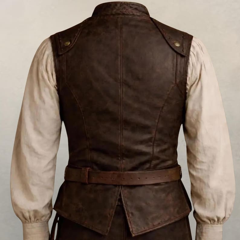 May include: A dark brown leather vest featuring a high collar, structured seams, and a matching leather belt at the waist. The vest is worn over a long-sleeved, off-white shirt with gathered cuffs. The design includes metallic buttons at the shoulders.