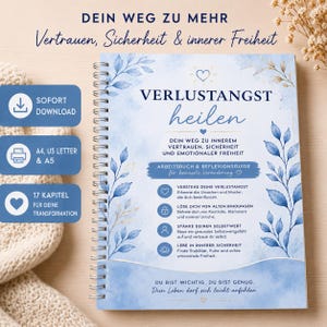 May include: A spiral-bound workbook with the title "VERLUSTANGST heilen" in a handwritten font. The cover features blue watercolor floral designs and text in German. The workbook includes the text "SOFORT DOWNLOAD" and "17 KAPITEL FÜR DEINE TRANSFORMATION".