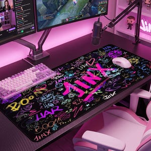 Può includere: Un tappetino da scrivania rettangolare nero con vivaci scarabocchi in stile graffiti color neon e la parola JINX in grandi lettere rosa. Il design include vari ghirigori, cuori e le scritte BOOM, HA HA HA e POWDER sulla superficie.