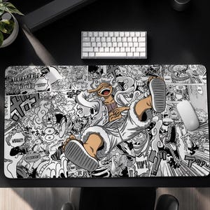 Pu&ograve; includere: Un tappetino per mouse rettangolare in bianco e nero con un'illustrazione in stile manga di un personaggio in abito bianco con un lungo naso e sandali. Lo sfondo &egrave; pieno di fumetti e fumetti. Sono visibili una tastiera e un mouse bianchi.