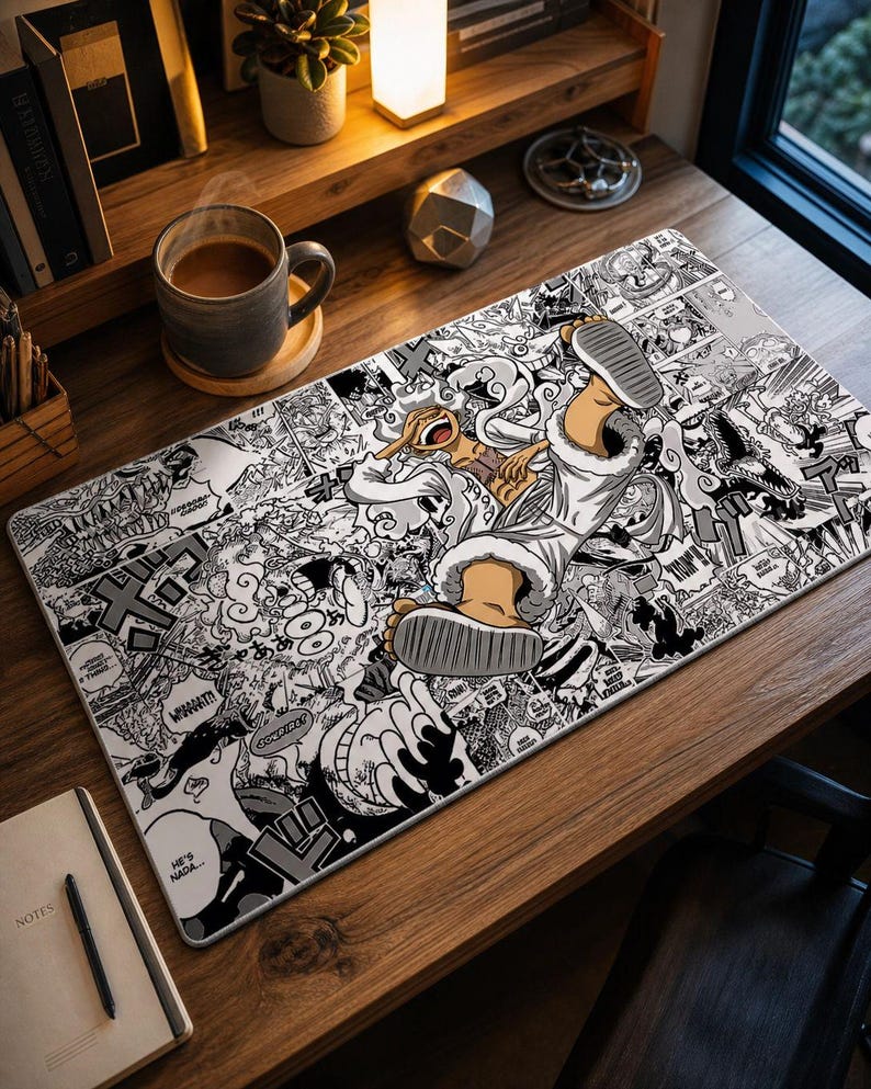 Pu&ograve; includere: Un tappetino da scrivania rettangolare in bianco e nero in stile manga con un personaggio con cappotto e stivali bianchi. Il tappetino &egrave; ricoperto da pannelli manga e fumetti. Una tazza di caff&egrave; e un taccuino sono sulla scrivania di legno.