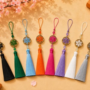Peut inclure: Huit ornements suspendus décoratifs dotés d'un cadre métallique circulaire avec une incrustation en forme de fleur en noir, vert, bleu, orange, rose, violet, blanc et gris, chacun attaché à un pompon en soie assorti et une fine boucle.
