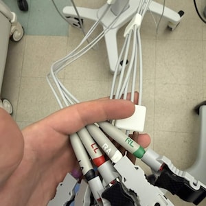 May include: A bundle of medical equipment cables with various colored connectors, including red, green, and black. The cables are held together and appear to be part of a medical device, likely used for monitoring or diagnostic purposes.