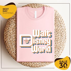 A pink t-shirt with the text "Walt Disney World" printed on it, placed on a woven basket. There are two yellow sale signs in the image, one on the left and one on the right, indicating a 30% discount on the item.