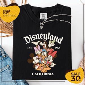 A black t-shirt with a Disney-themed graphic and text, along with a yellow price tag and a denim item, suggesting a sale or promotional event related to the t-shirt.