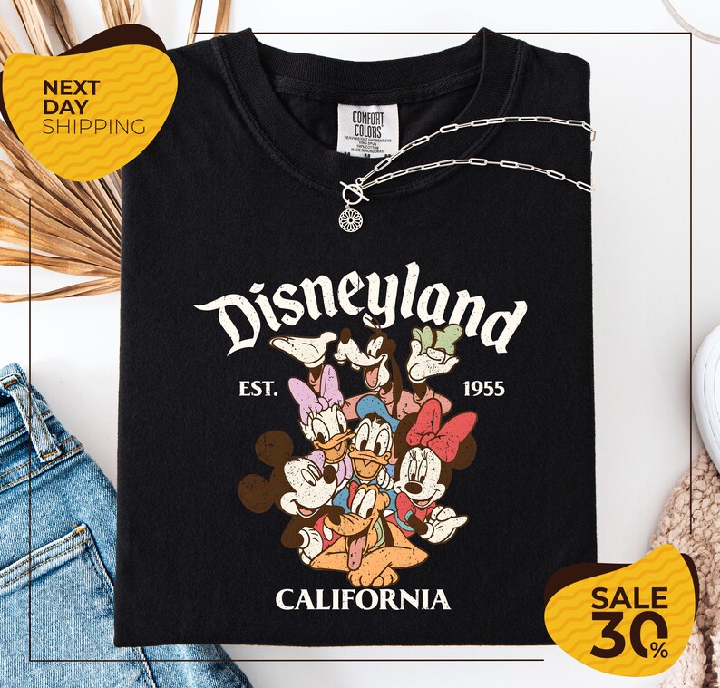 A black t-shirt with a Disney-themed graphic and text, along with a yellow price tag and a denim item, suggesting a sale or promotional event related to the t-shirt.