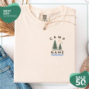 a white t-shirt with a graphic design, a necklace, and some clothing items, including a pair of jeans, on a white background.