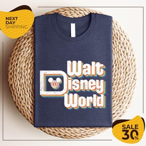 A navy blue t-shirt with the text "Walt Disney World" printed on it, along with a Mickey Mouse logo, is displayed on a woven basket. The image also includes text indicating a sale with a 30% discount.