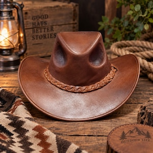 Könnte beinhalten: Ein brauner Leder-Cowboyhut mit einer eingedrückten Krone und einem geflochtenen Lederhutband. Der Hut hat eine breite, geschwungene Krempe und eine glatte, strukturierte Oberfläche, die ein klassisches Western-Design mit sichtbaren Nähten zeigt.