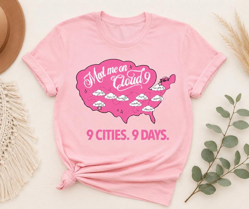 May include: A light pink t-shirt featuring a pink map graphic with the text "Meet me on Cloud 9" and "9 Cities. 9 Days." The map includes cloud illustrations and city names. The shirt has short sleeves and a crew neck.