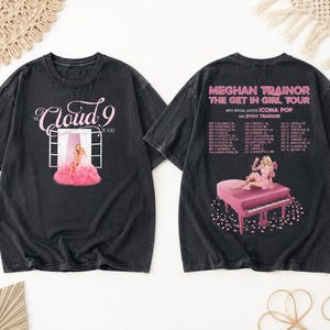 May include: Black t-shirts featuring a pink graphic of a woman on a piano and the text "MEGHAN TRAINOR THE GET IN GIRL TOUR". The front of the shirt has the text "Cloud 9 TOUR" with a pink graphic.