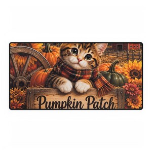 Può includere: Un tappetino decorativo rettangolare con un gattino tigrato marrone che indossa una sciarpa a quadri, appoggiato su una cassa di legno con la scritta Pumpkin Patch. La scena include zucche arancioni, girasoli e un fienile rosso sullo sfondo.
