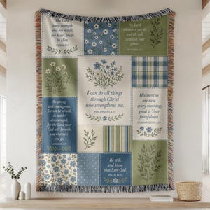 May include: A woven throw blanket featuring a patchwork design of blue, green, and cream panels. The panels display floral illustrations, plaid and striped patterns, and religious scripture text including Philippians 4:13 and Psalm 46:10.
