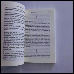 May include: An open book with white pages and black printed text. The left page is titled The Power of Now, page 50, and the right page is titled Moving Deeply into the Now, page 53, with the heading The Key to the Spiritual Dimension.