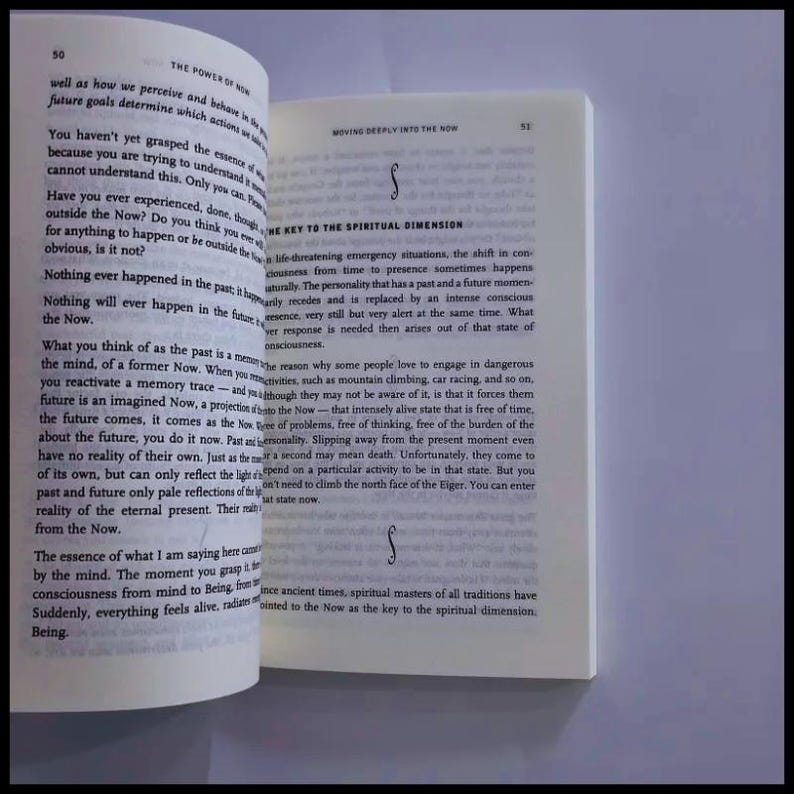May include: An open book with white pages and black printed text. The left page is titled The Power of Now, page 50, and the right page is titled Moving Deeply into the Now, page 53, with the heading The Key to the Spiritual Dimension.