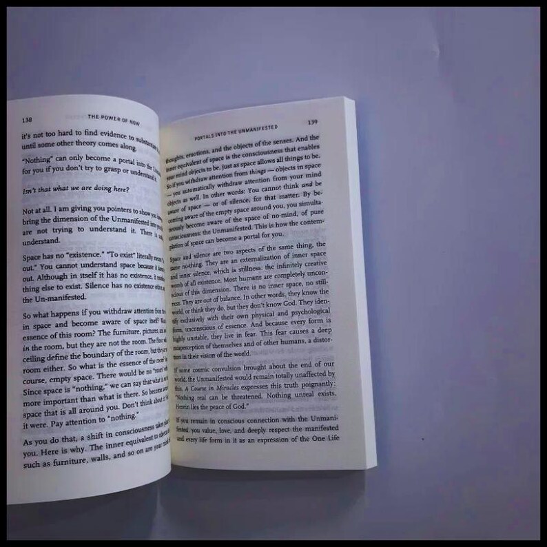 May include: An open book with white pages and black printed text. The left page is numbered 138 and titled The Power of Now, while the right page is numbered 139 and titled Portals into the Unmanifested. The text discusses consciousness, space, and silence.