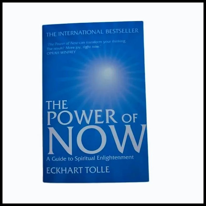 May include: A blue book titled The Power of Now by Eckhart Tolle. The cover features a bright light radiating from the center, with the text The International Bestseller and a quote by Oprah Winfrey, A Guide to Spiritual Enlightenment.