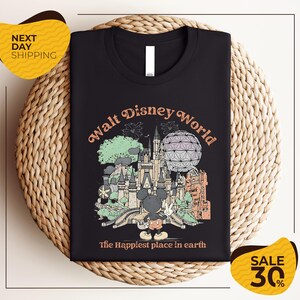 A black t-shirt with a graphic design depicting various Disney landmarks and elements, including Mickey Mouse and the Eiffel Tower, along with the text "Walt Disney World" and "The Happiest place in earth".