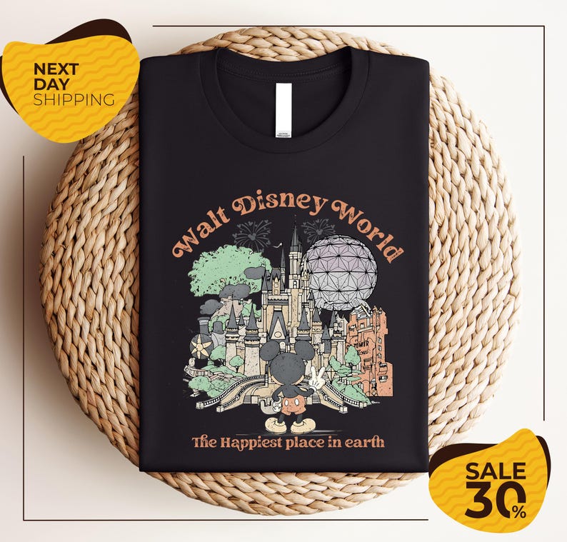 A black t-shirt with a graphic design depicting various Disney landmarks and elements, including Mickey Mouse and the Eiffel Tower, along with the text "Walt Disney World" and "The Happiest place in earth".