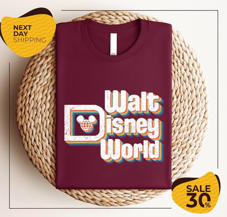 a maroon t-shirt with the text "Walt Disney World" printed on it, along with a Mickey Mouse logo. The t-shirt is displayed on a woven basket, and there are two yellow price tags in the image.