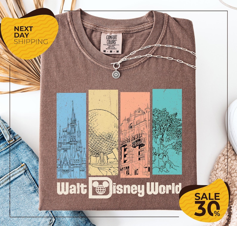 a brown t-shirt with a graphic design of Disney World landmarks, including a castle, roller coaster, and other iconic structures. The t-shirt is displayed on a white background, and there are two yellow sale signs indicating a 30% discount on the item.