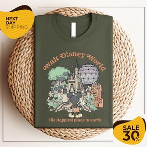 A green t-shirt with a graphic design of various Disney landmarks and characters, including Mickey Mouse, the Eiffel Tower, and the Space Needle, along with the text "Walt Disney World" and "The Happiest place in earth".