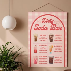 May include: A pink and white checkered Dirty Soda Bar sign with a retro design. The sign lists various soda concoctions with ingredients like Diet Coke, vanilla syrup, and coconut creamer. The sign is hanging on a wall.