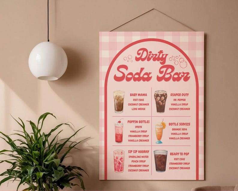 May include: A pink and white checkered Dirty Soda Bar sign with a retro design. The sign lists various soda concoctions with ingredients like Diet Coke, vanilla syrup, and coconut creamer. The sign is hanging on a wall.