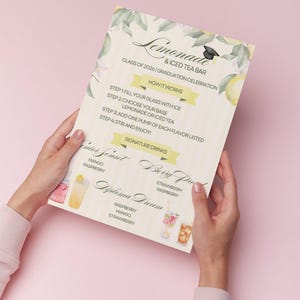 Op de afbeelding: Een afstudeer-thema menu voor een limonade- en ijsthee bar, vastgehouden door handen tegen een roze achtergrond. Het menu bevat een bloemenontwerp, drankrecepten en de tekst "Klasse van 2026 | Afstudeerfeest".